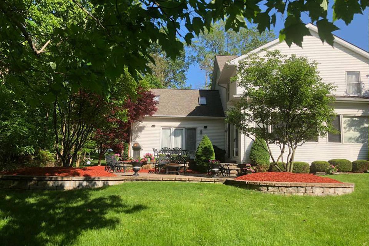 A white house with a large lawn in front of it surrounded by trees.