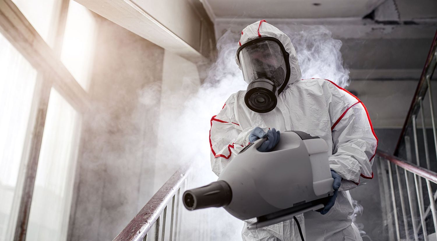 Person in hazmat suit disinfecting a stairway with a fog machine.