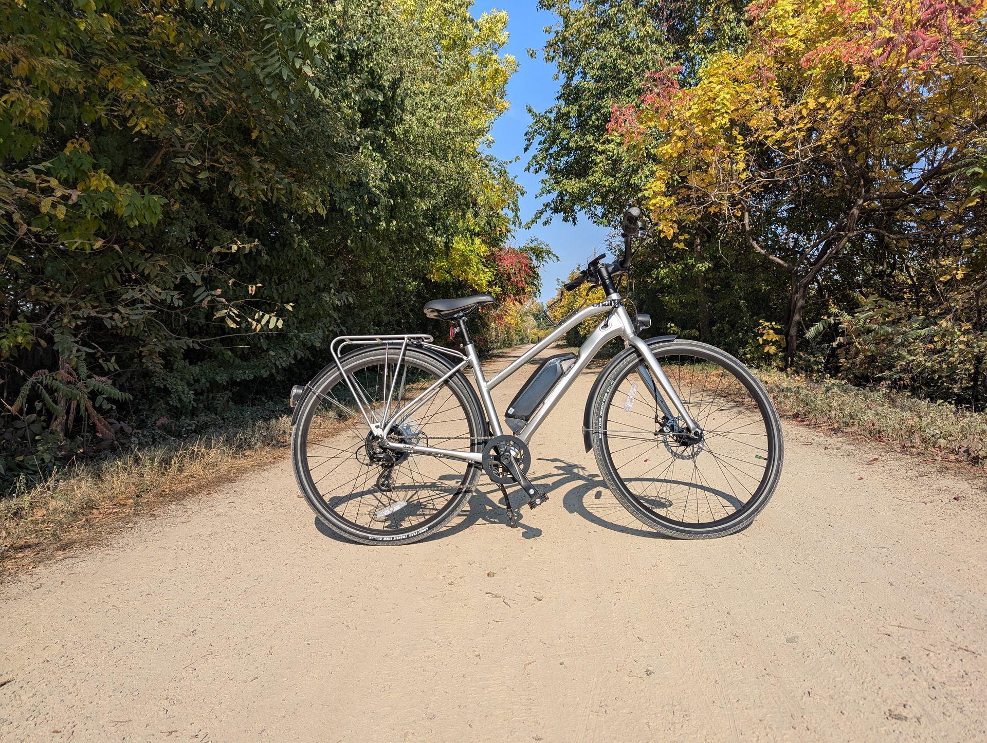 A bicycle is parked on the side of a dirt road.