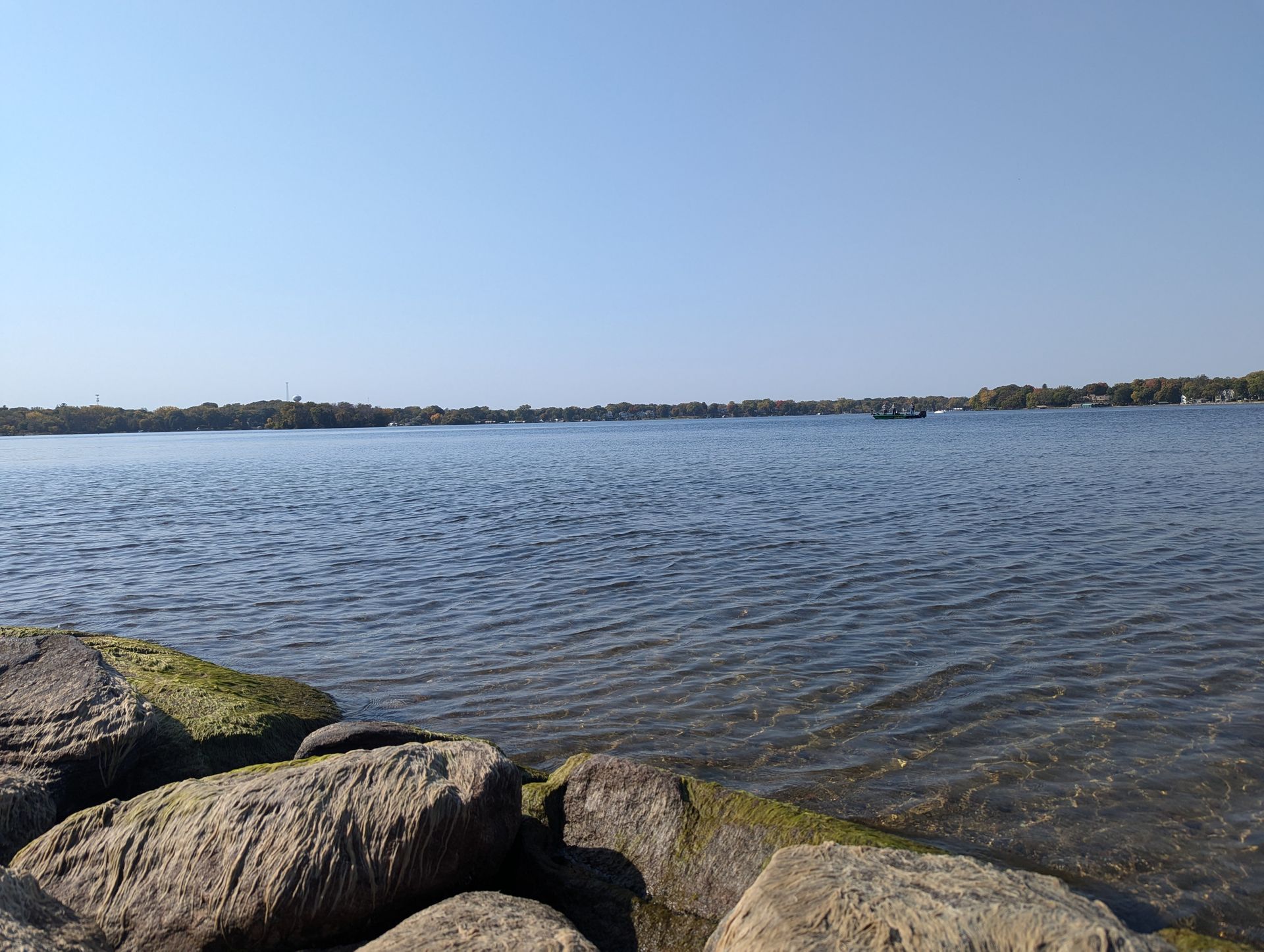 A large body of water with rocks in the foreground and trees in the background.