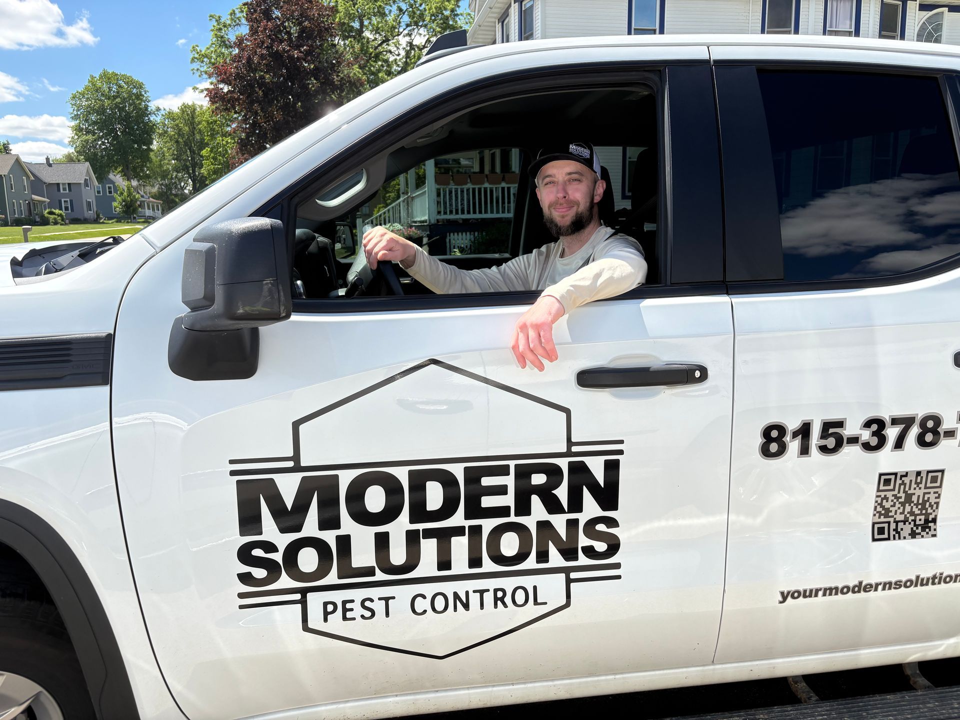 Driver in white Modern Solutions Pest Control truck, arm resting out window, with logo visible on the door.