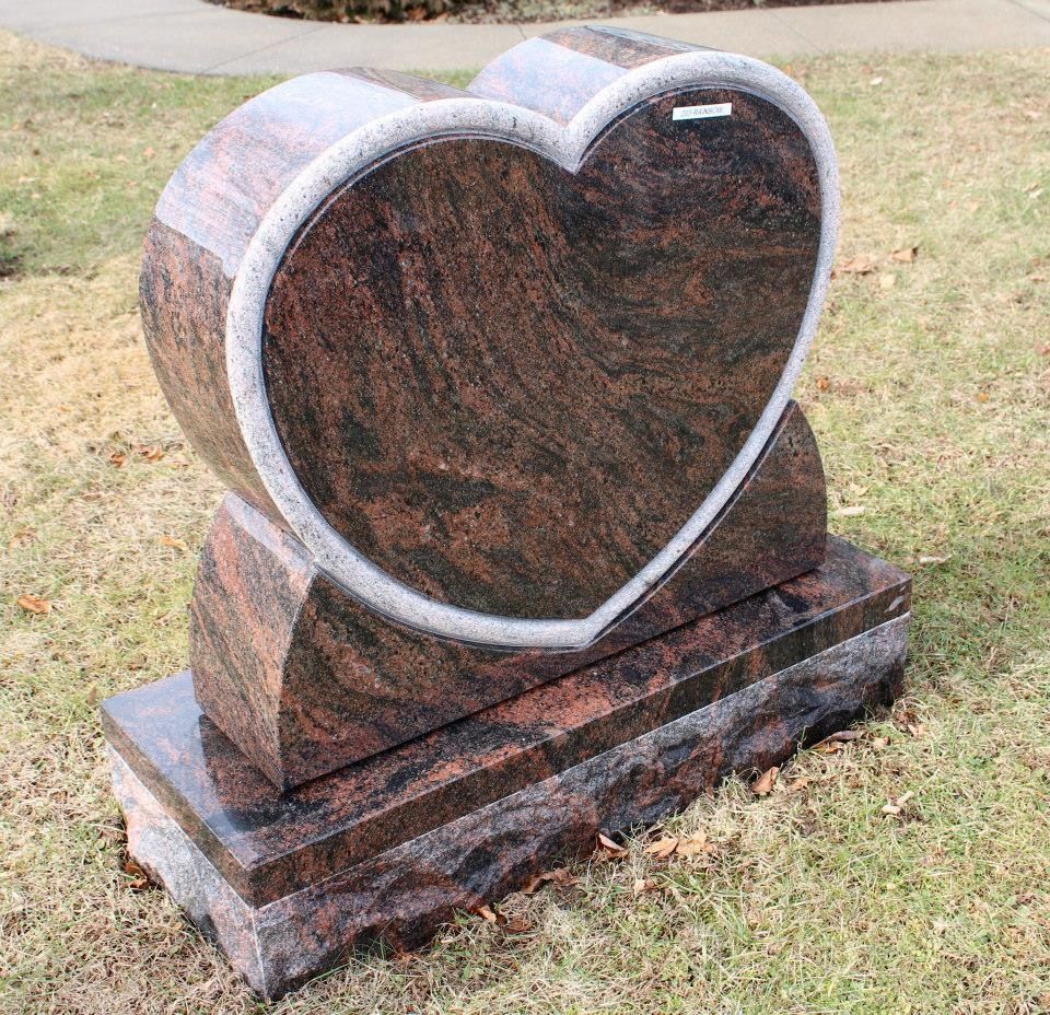 A gravestone in the shape of a heart is sitting in the grass.