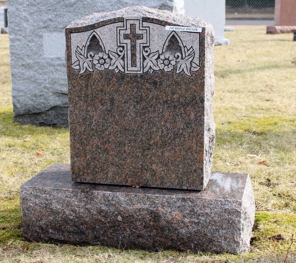 A gravestone with a cross and flowers on it is in a cemetery.
