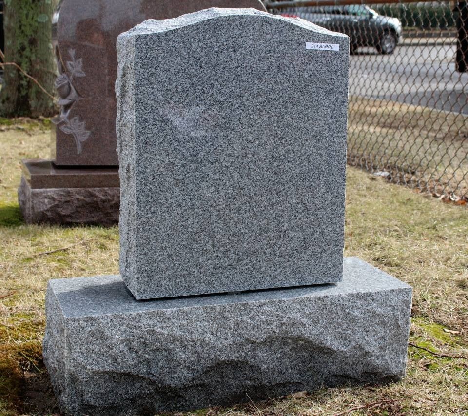 A gravestone is sitting in the grass in front of a chain link fence.