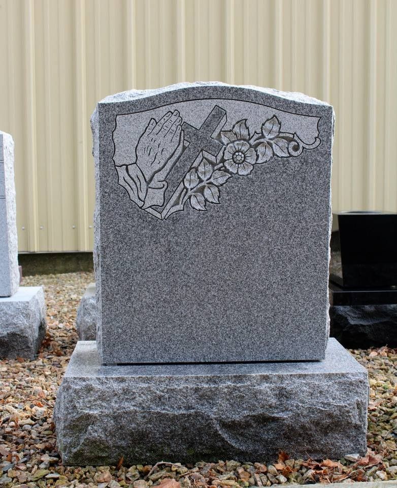 A gravestone with praying hands and flowers on it