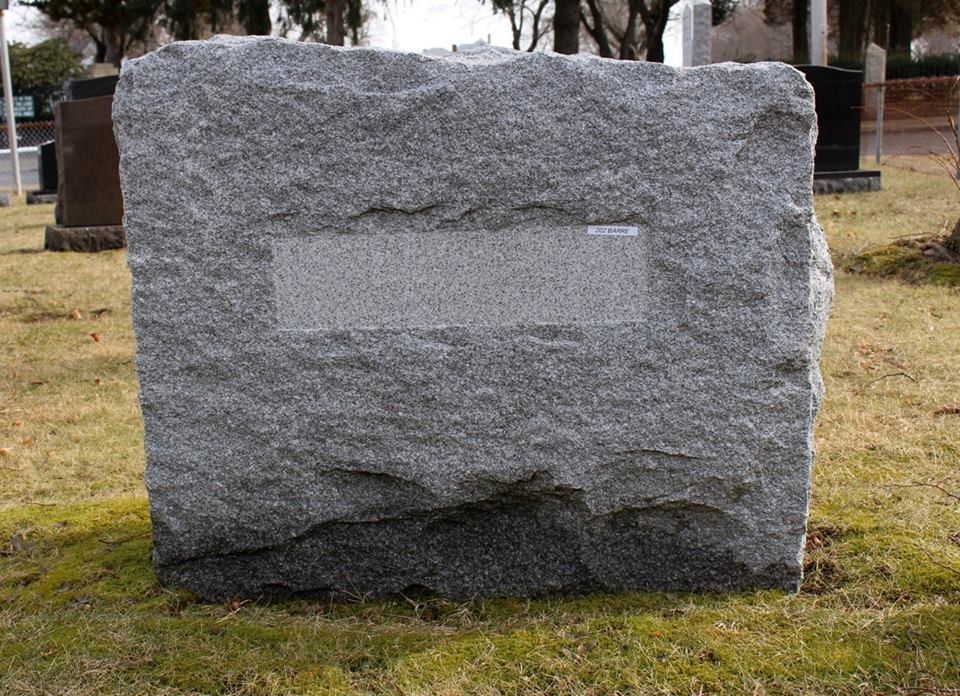 A large granite gravestone is sitting in the grass in a cemetery.