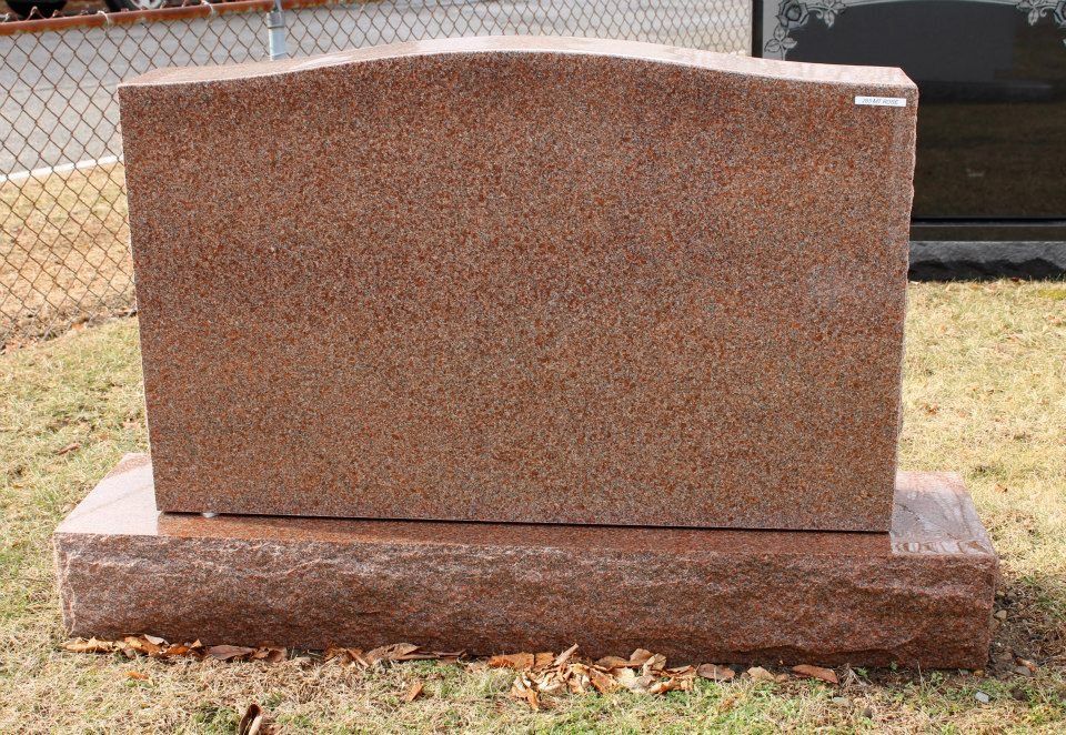 A gravestone is sitting in the grass in front of a chain link fence.