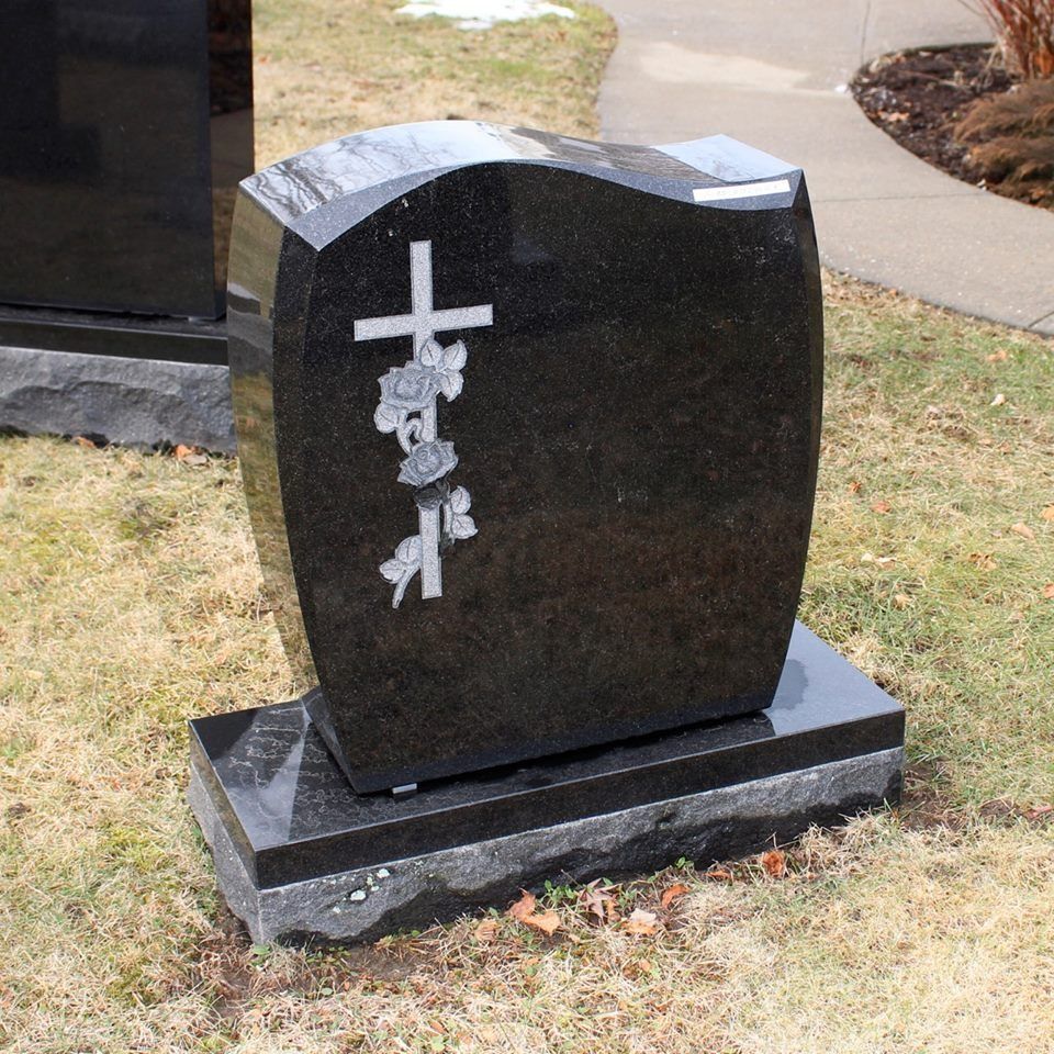 A black gravestone with a cross and flowers on it