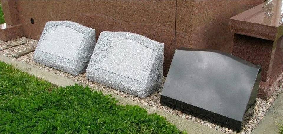 Three grave stones are sitting in the grass in front of a building.