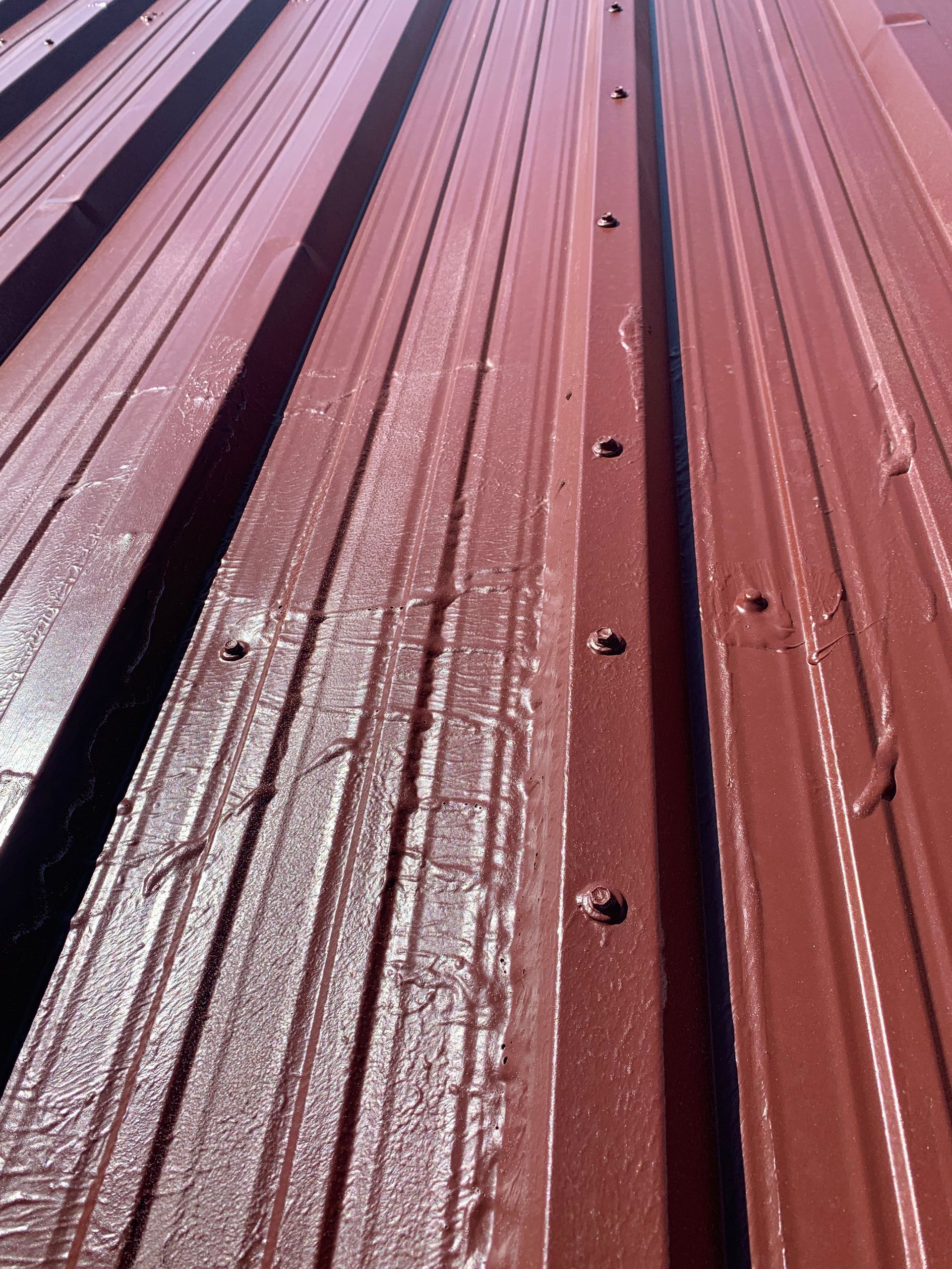 A close up of a red metal roof with screws in it
