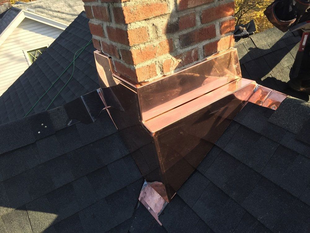 Copper flashing installed around a brick chimney on a shingled roof.