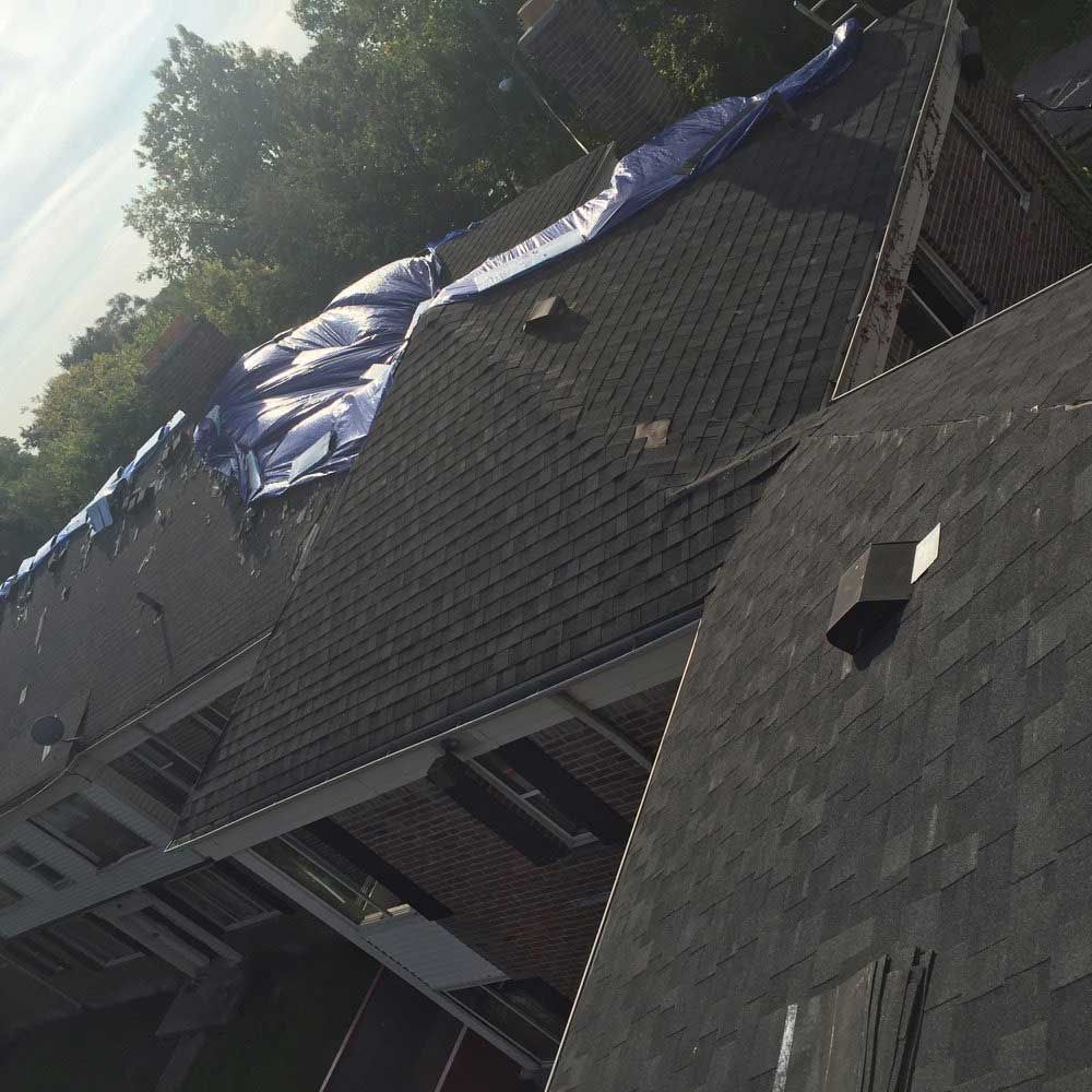 A high-angle view of a shingled roof with a large blue tarp covering a damaged section.