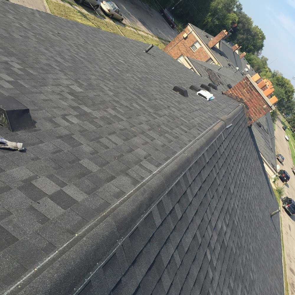 A high-angle view looking down the sloped surface of a dark gray shingled roof towards a parking lot below.