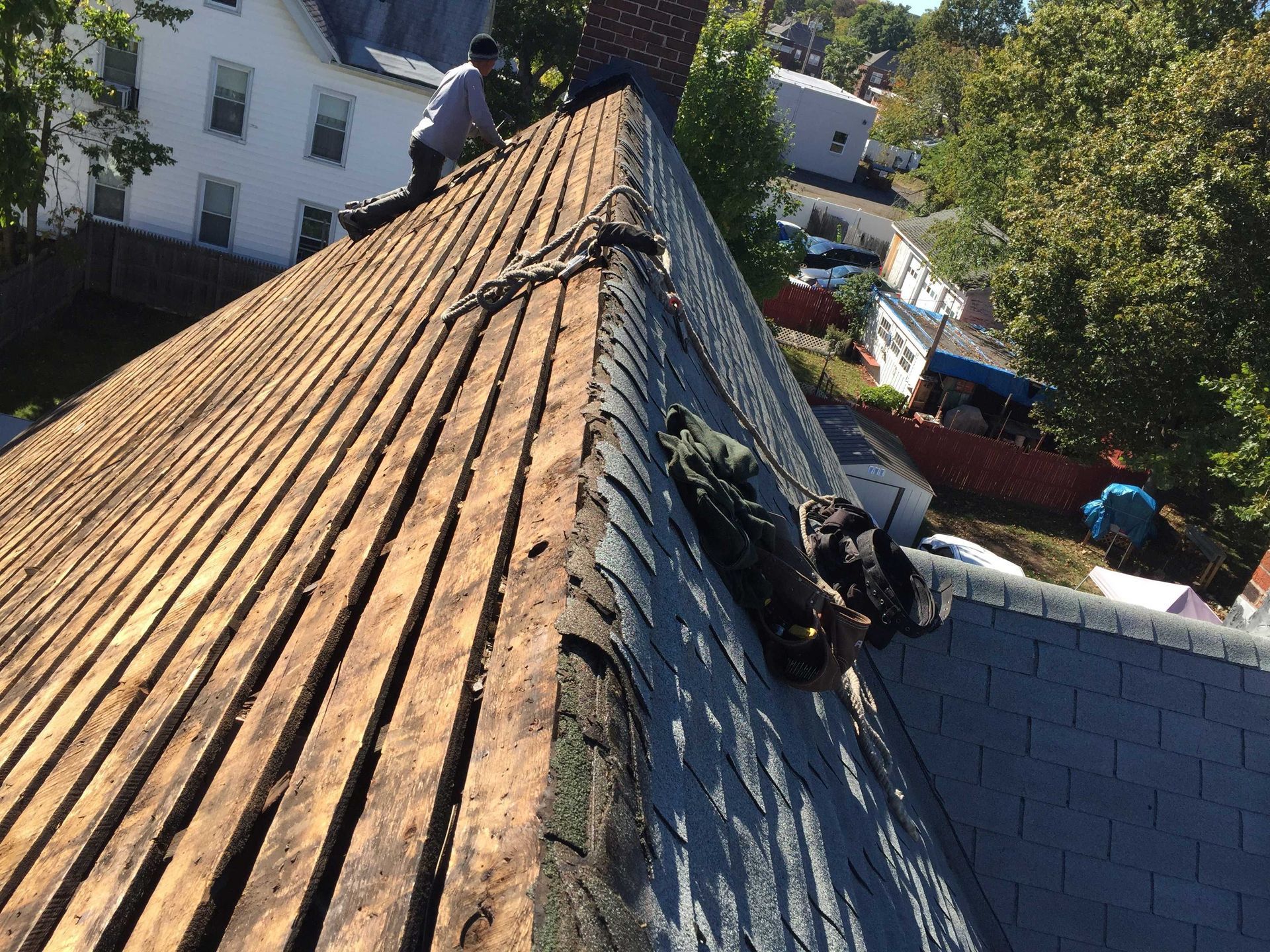 A worker installs wooden slats on a residential roof during a renovation, with partially shingled sections nearby.