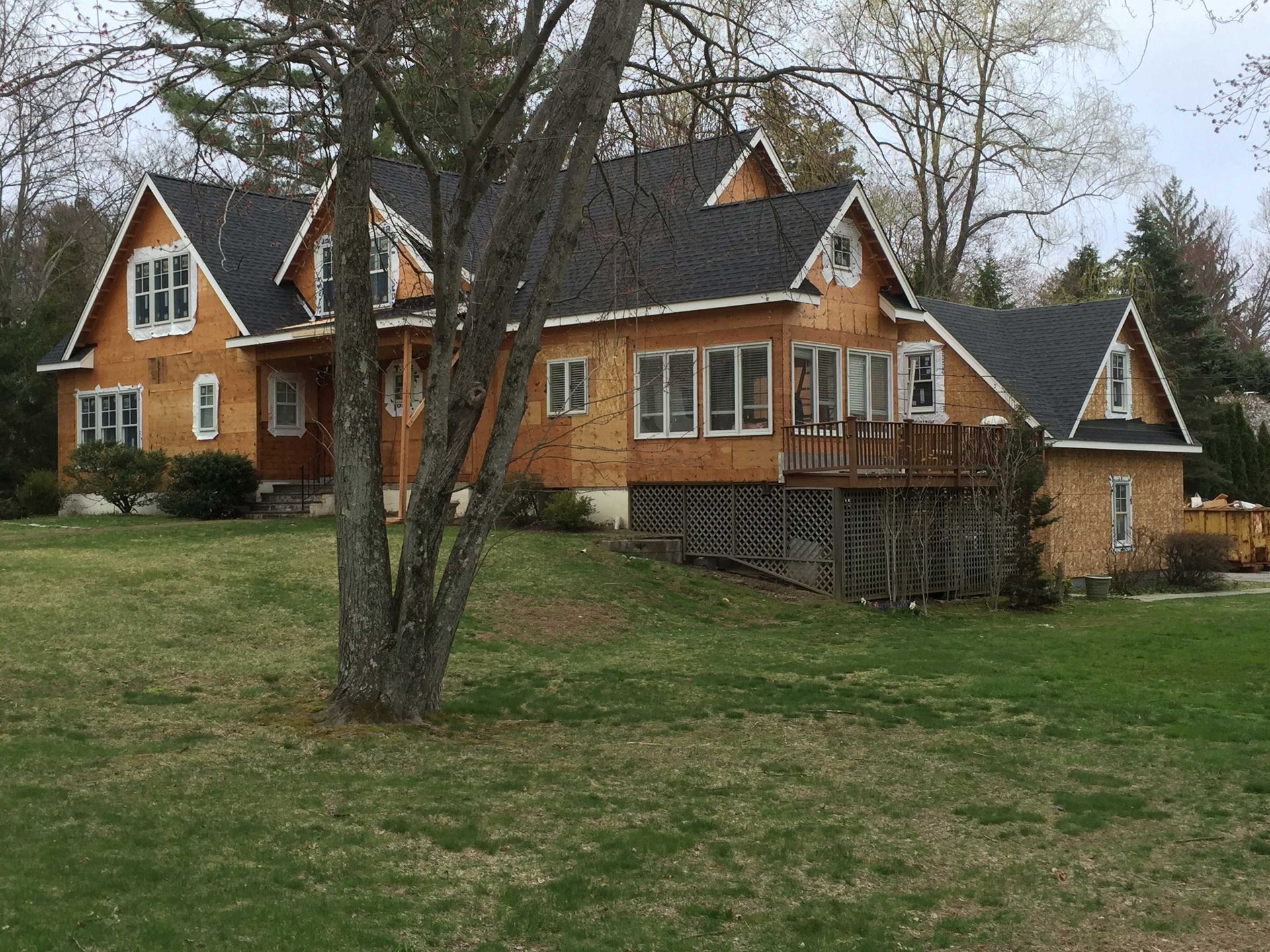 A large wooden house with multiple gables and dark shingles, situated on a grassy lawn with surrounding trees.