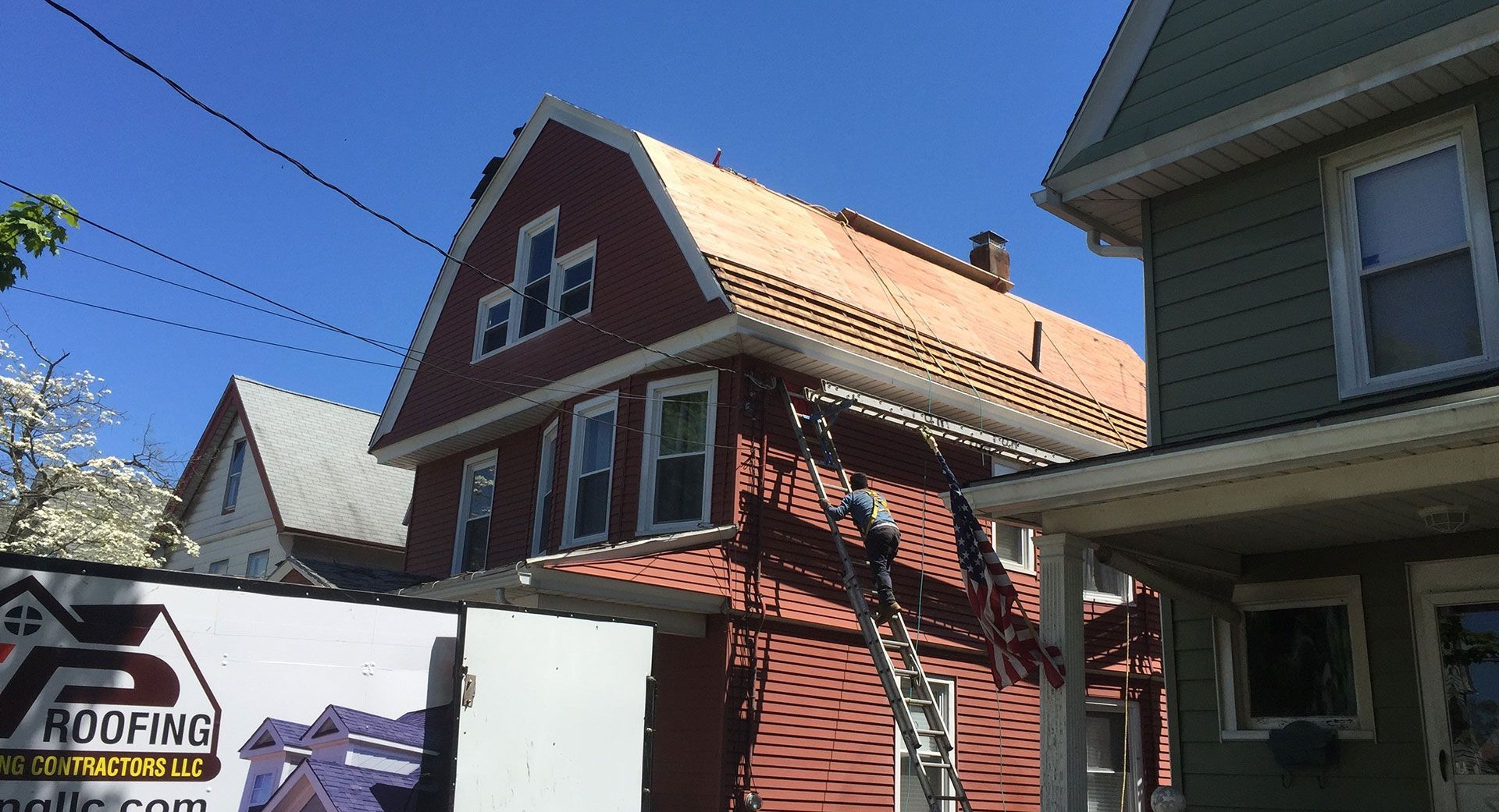 Roofers working on the shingles of a red house with a large roof replacement in progress on a sunny day.