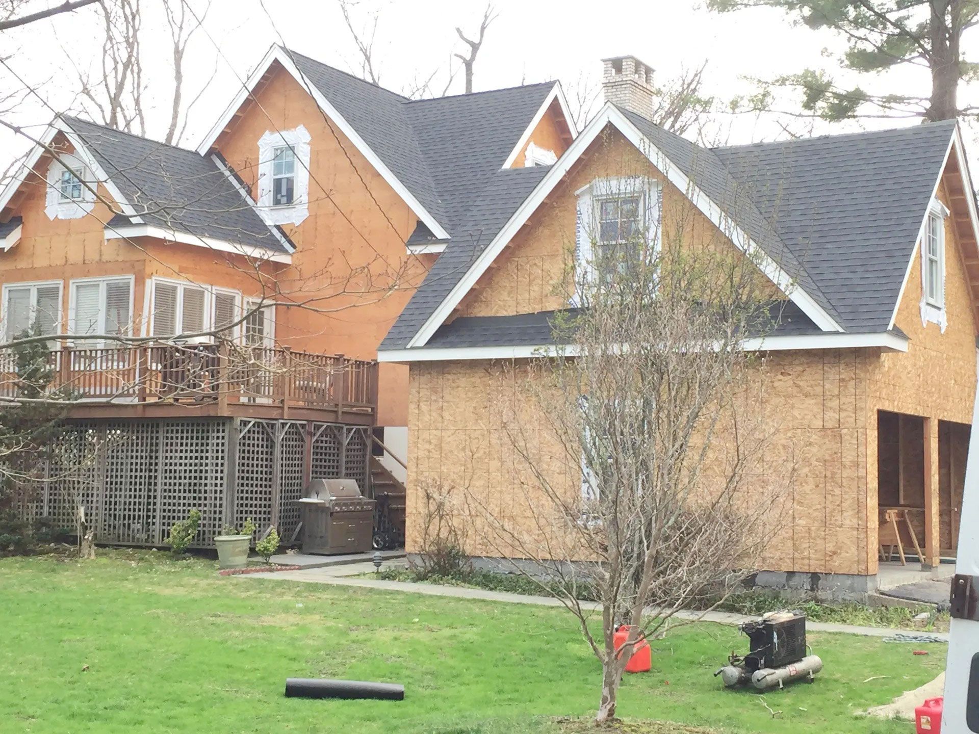 A residential home under construction featuring unfinished wooden exterior walls and new dark shingled roofs.