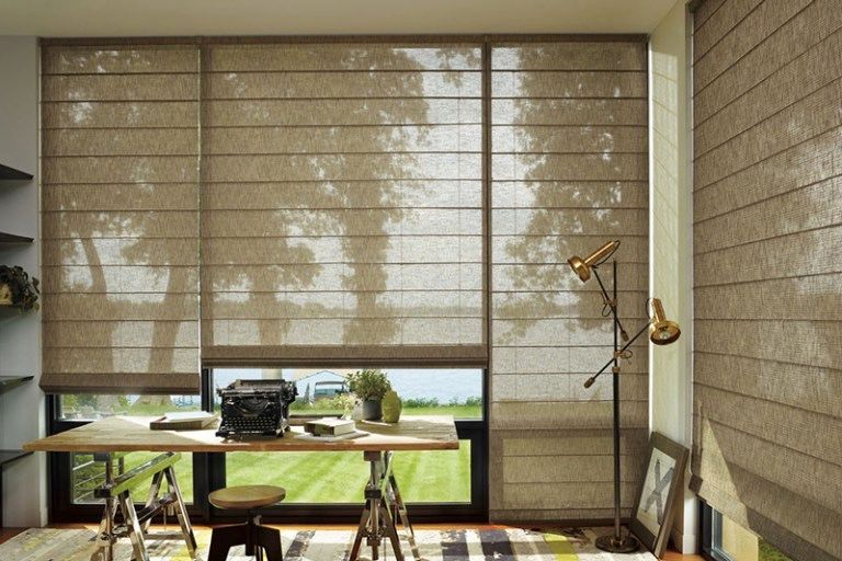 A room with a desk and a window with roman shades