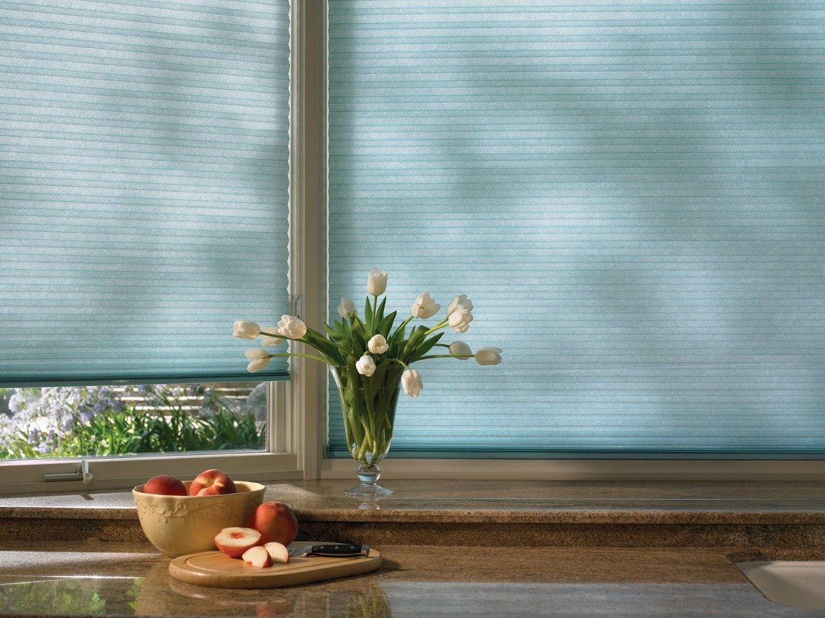 A vase of flowers is sitting on a counter in front of a window.