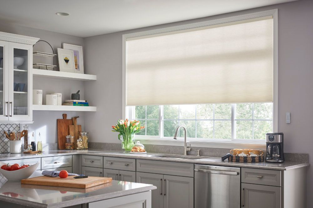 A kitchen with white cabinets and a large window with blinds.