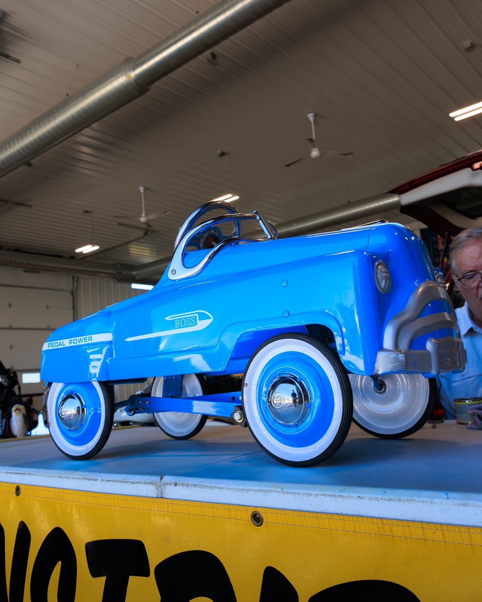 Bright blue vintage toy car on a display platform in a garage-like setting