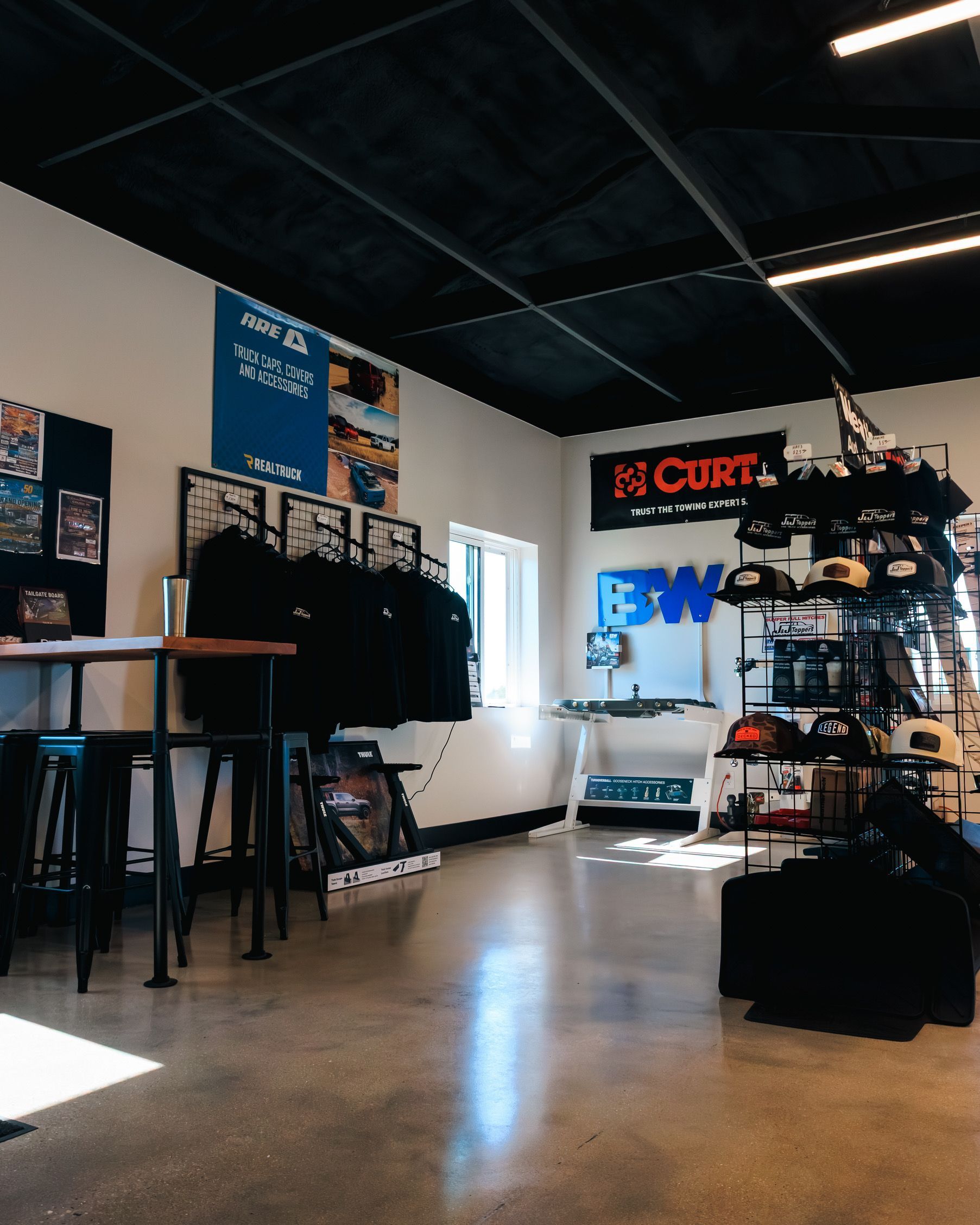 Small boutique studio with hanging clothes, posters, and industrial lights, viewed across a polished floor.
