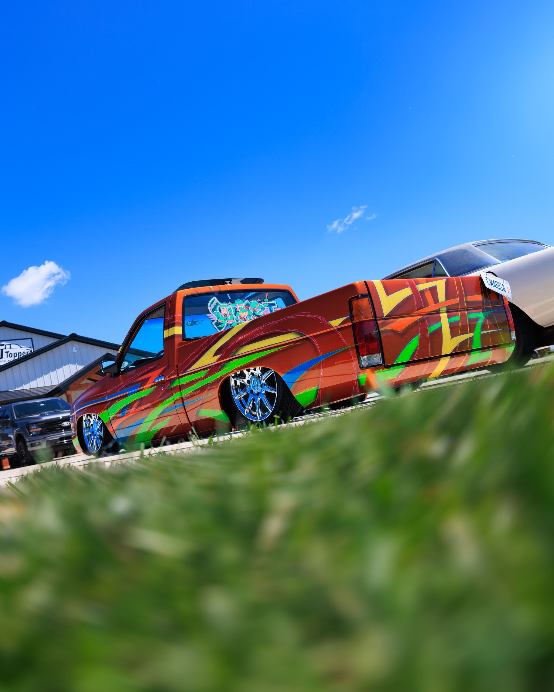 Colorfully painted lowrider pickup truck on grass under a bright blue sky