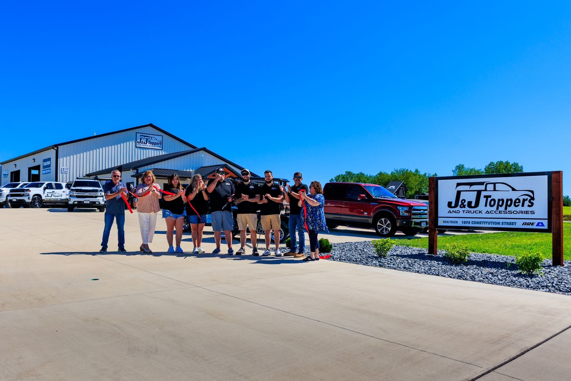 Group of people outside a Just Toppers building and sign on a sunny day
