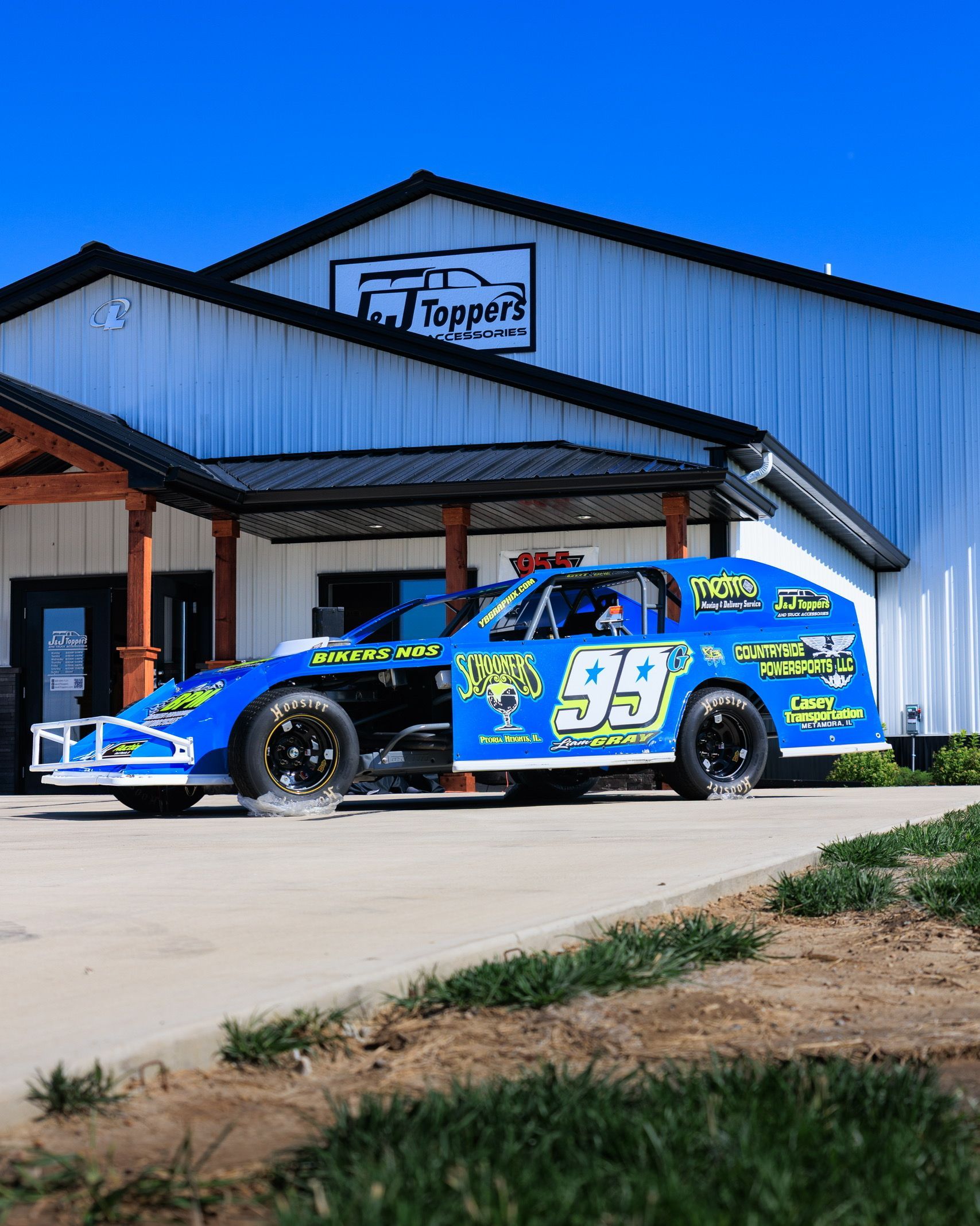 Blue race car parked outside a metal building with a sign above the entrance.