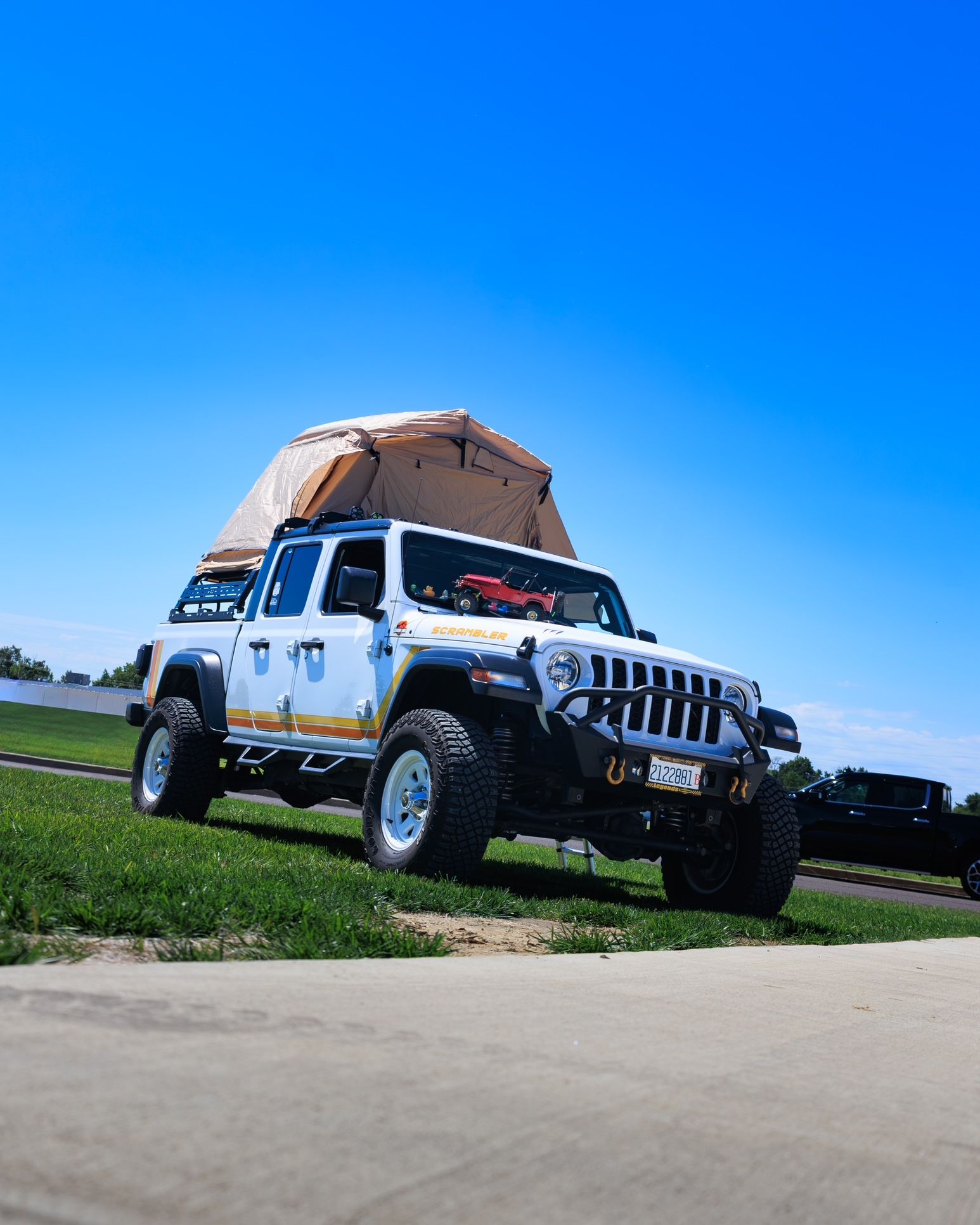 White off-road Jeep with roof tent parked on grass under a clear blue sky.