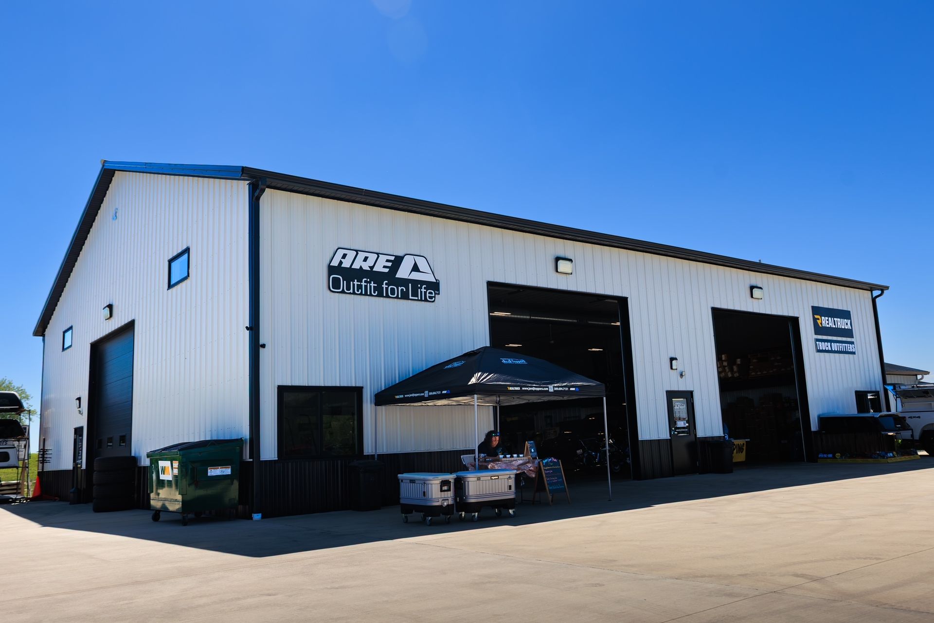 White industrial building with black trim and open garage bays under a clear blue sky