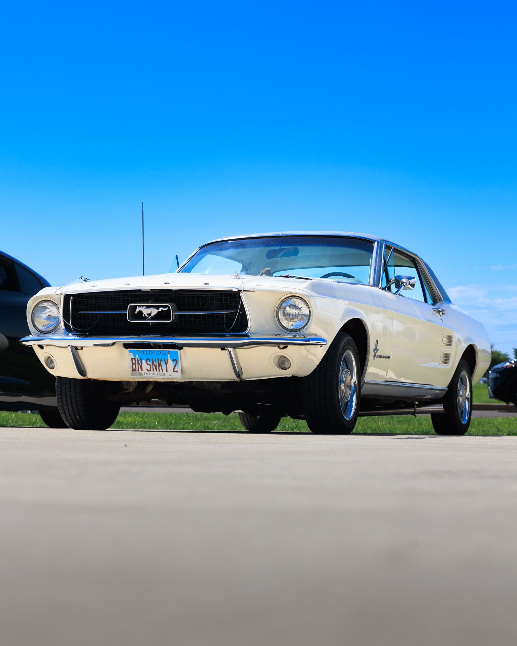 Cream-colored classic Ford Mustang parked on a driveway under a bright blue sky