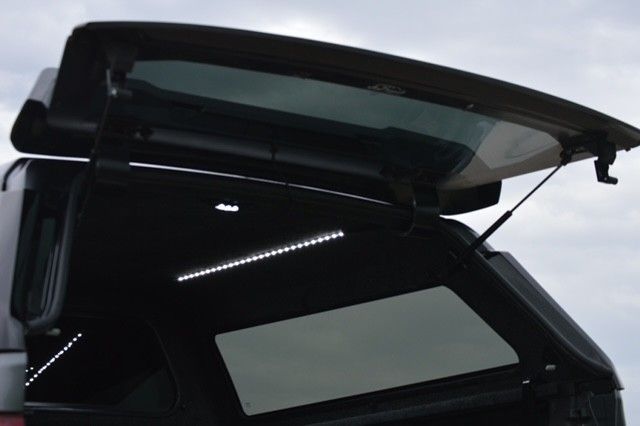 Open car rear hatch with glass spoiler raised against a cloudy sky