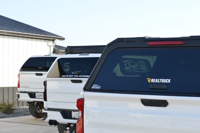 Three white pickup trucks parked beside a building under a bright sky