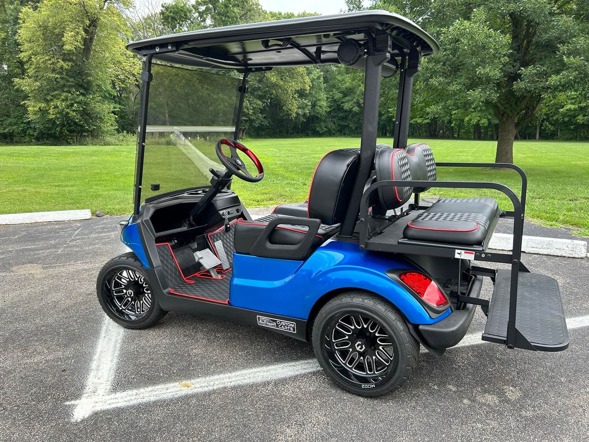 Blue golf cart with black accents, parked on asphalt, and surrounded by trees.