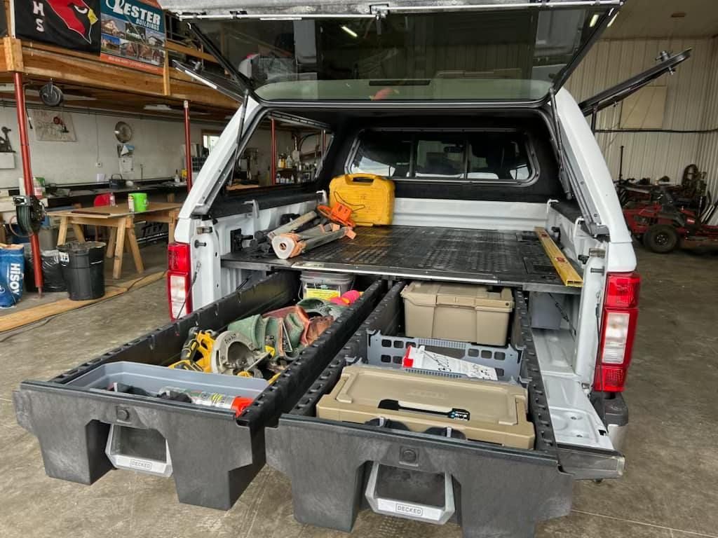 White pickup truck bed with open drawers holding tools and equipment.