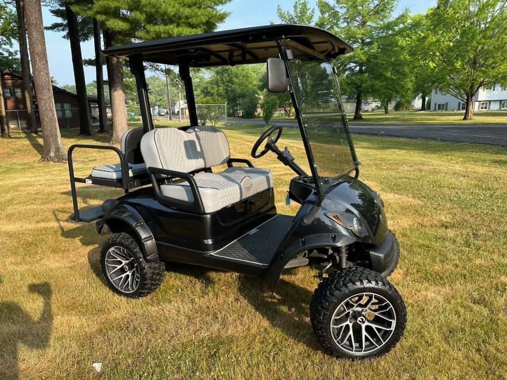Black golf cart with upgraded wheels, gray seats, and black canopy on grass.