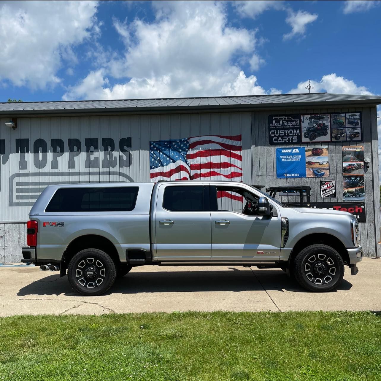 Silver pickup truck with a cap parked in front of a building with an American flag mural.