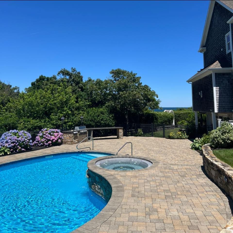 Outdoor patio with pool, hot tub, and house on a sunny day.