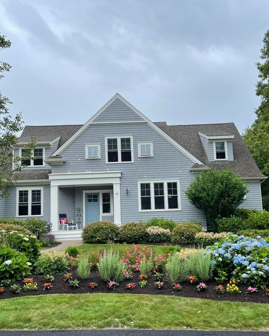 Gray house with blue door and flower garden.