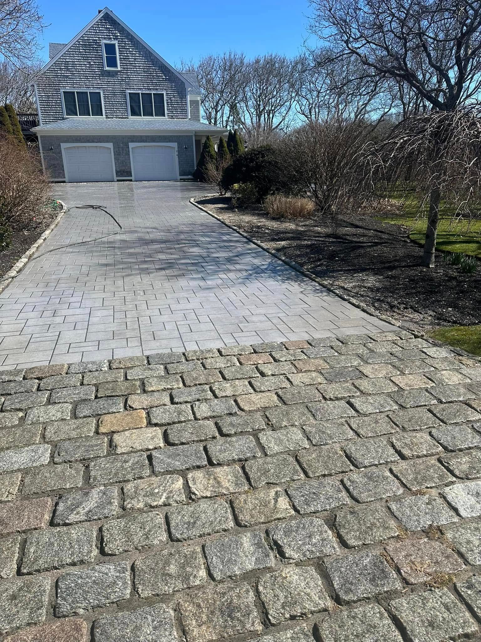 Driveway paved with cobblestones and rectangular stone leading to a house with a gray exterior and two-car garage.