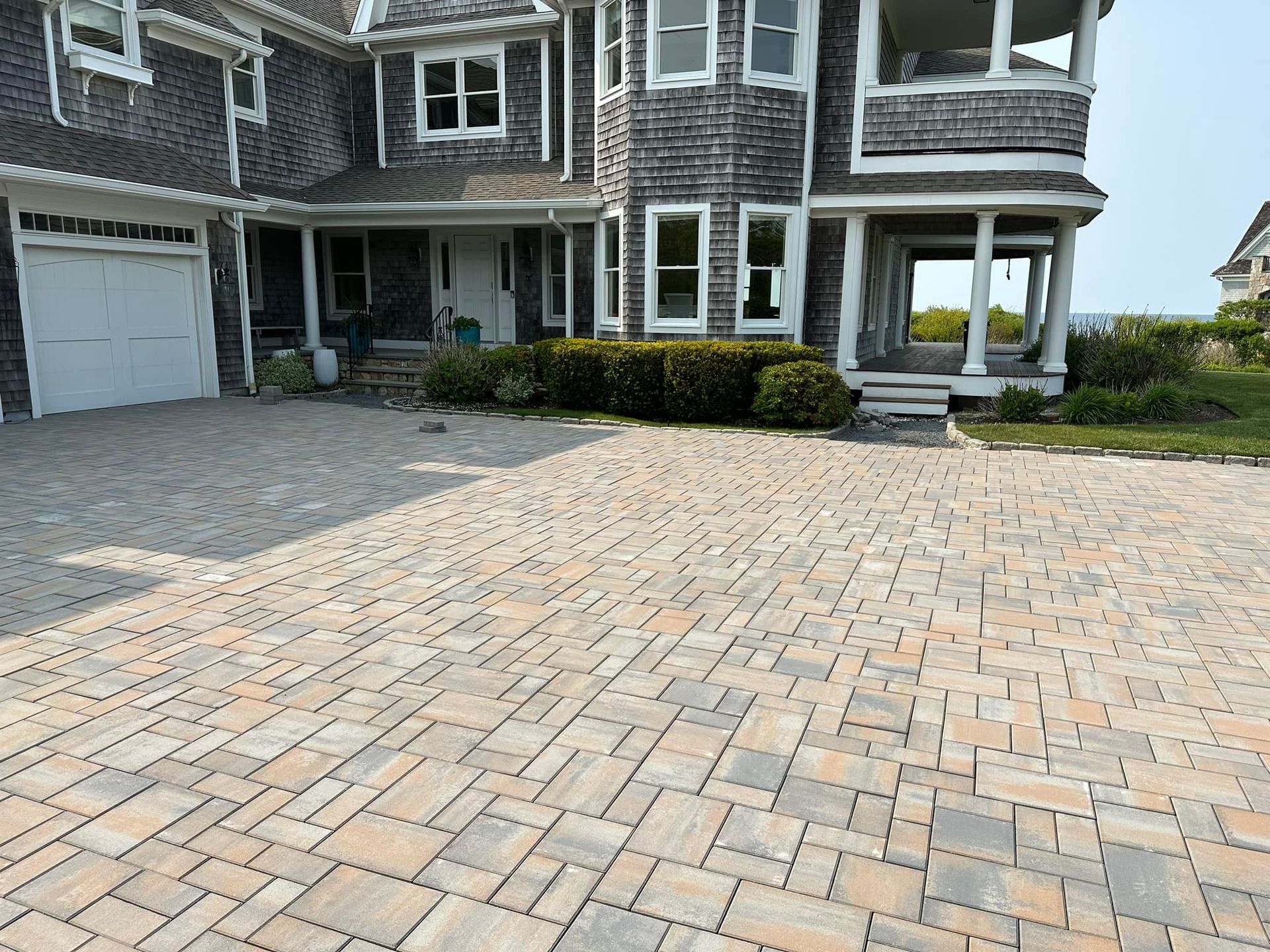 Large house with a brick driveway, light brown and gray bricks, gray siding and white trim.