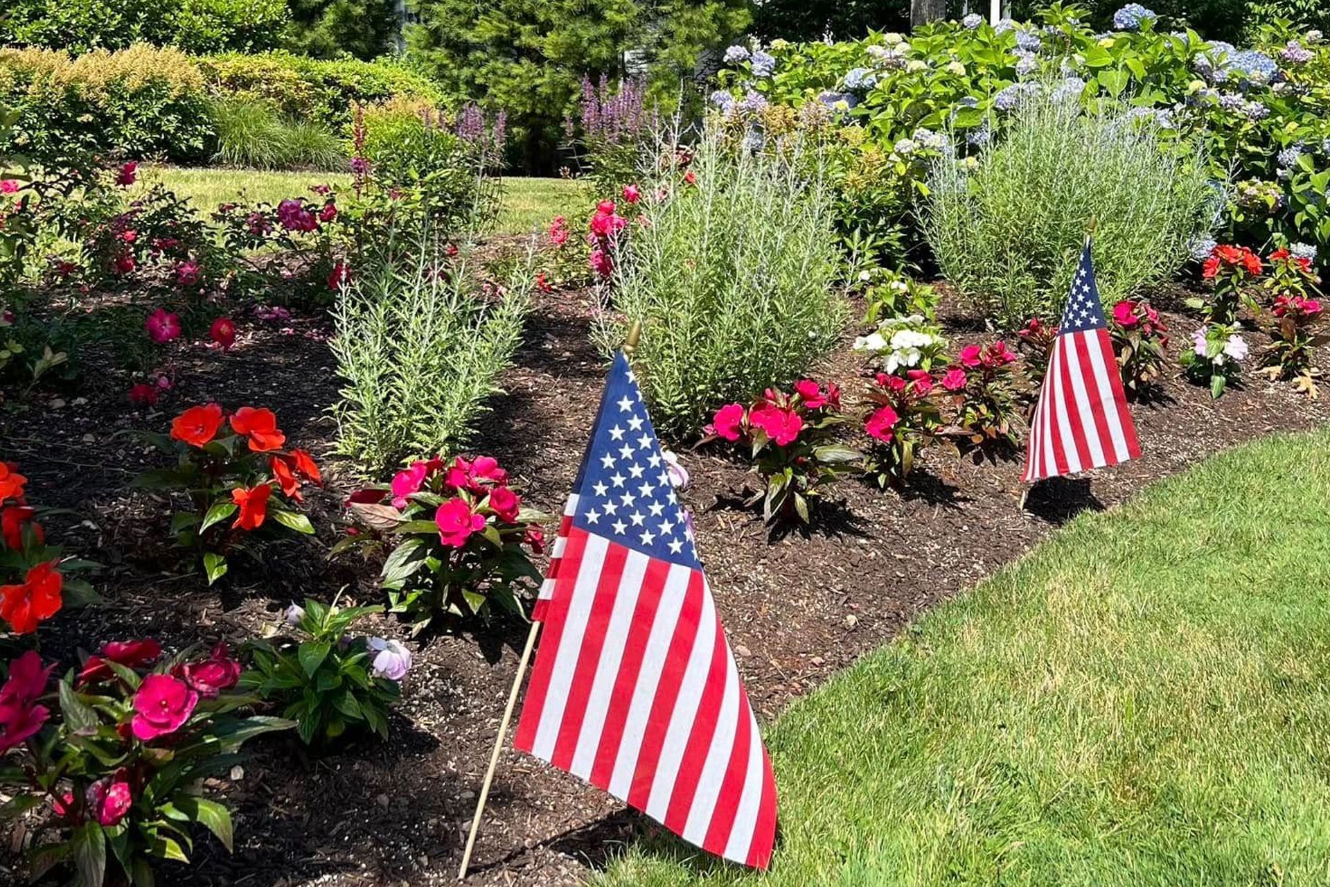 Sprinkler irrigates a green lawn in front of bushes and trees under a cloudy sky.