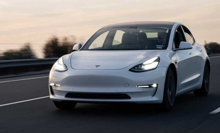 White Tesla Model 3 driving on a highway at dusk.