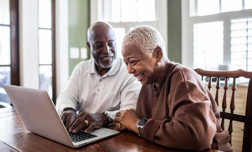 Older adults smiling at laptop screen indoors.