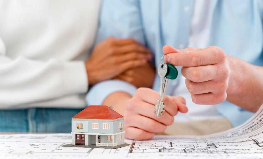 Couple holding keys with house model and blueprints.