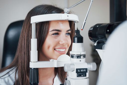 Woman smiling during an eye exam with a slit-lamp microscope at an optometrist's office