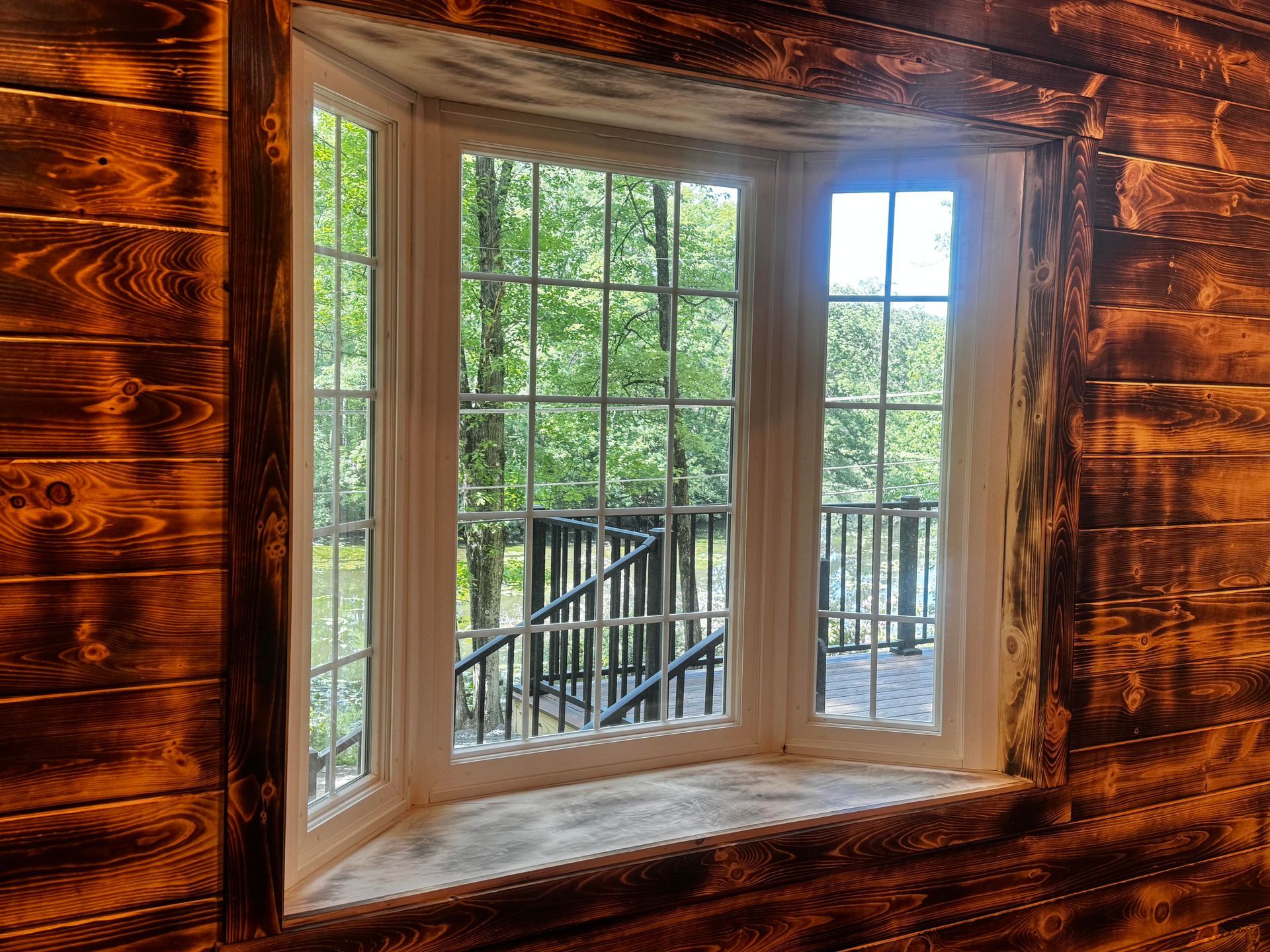 A bay window in a wooden wall with a view of trees