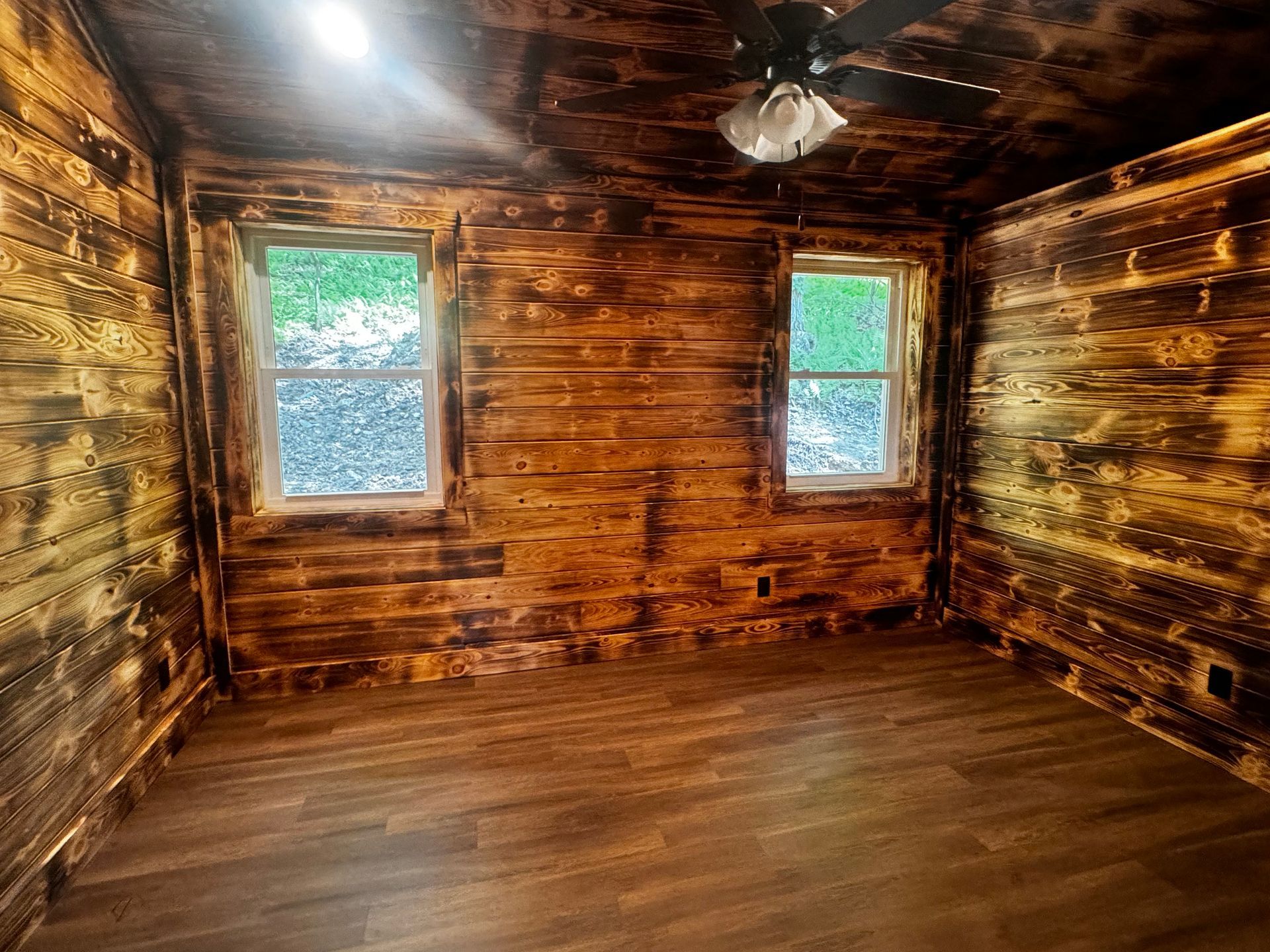 An empty room with wooden walls and a ceiling fan.