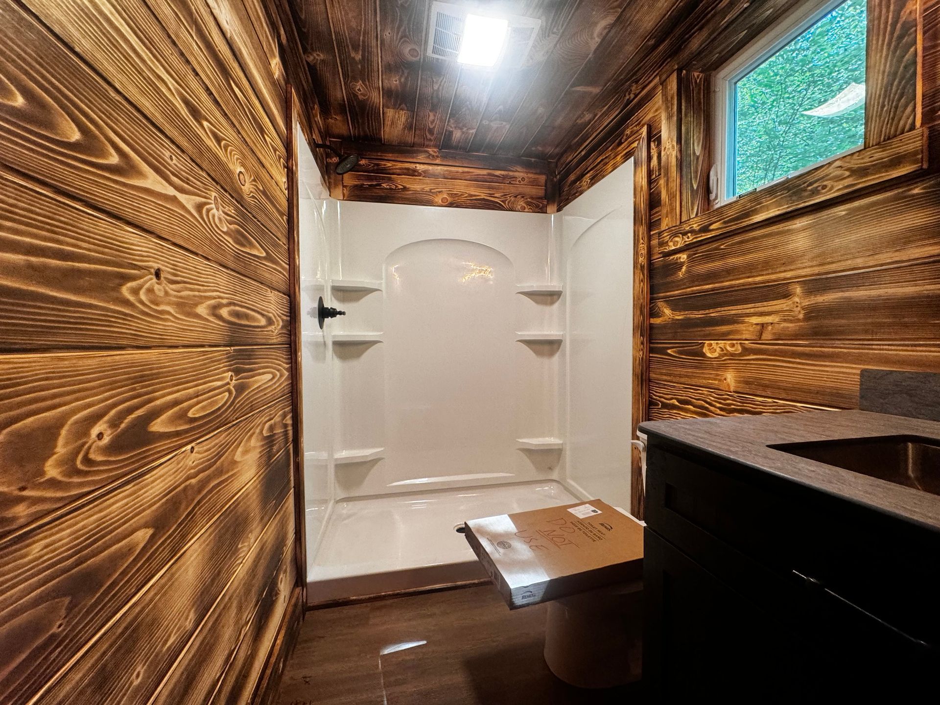 A bathroom with wooden walls , a toilet , and a shower.